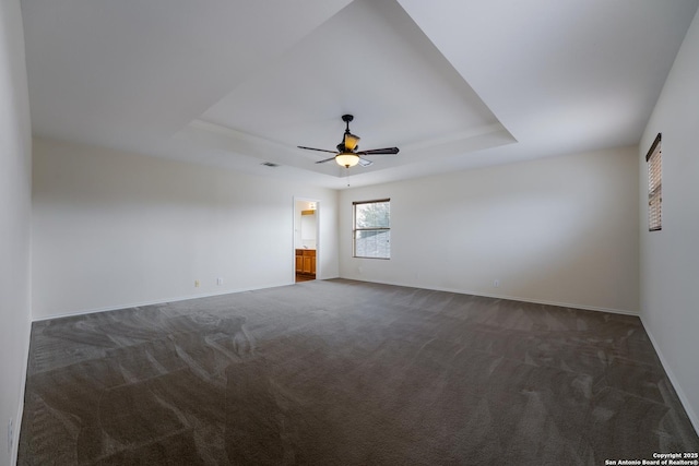 spare room featuring a raised ceiling, dark colored carpet, and ceiling fan