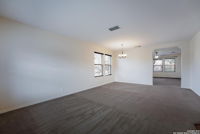 unfurnished room featuring dark colored carpet, ceiling fan with notable chandelier, and a wealth of natural light