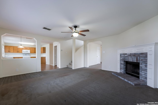 unfurnished living room featuring ceiling fan, dark carpet, and a brick fireplace