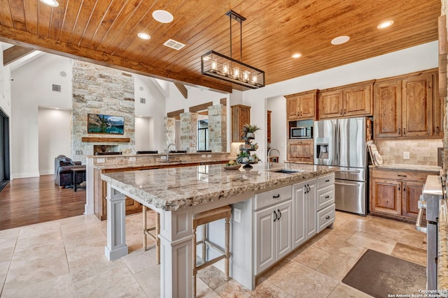 kitchen with appliances with stainless steel finishes, a fireplace, a kitchen breakfast bar, light stone counters, and a spacious island