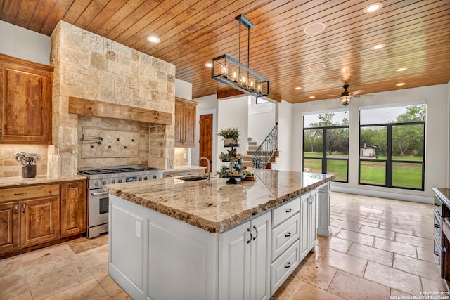 kitchen featuring sink, high end stove, an island with sink, white cabinets, and decorative light fixtures