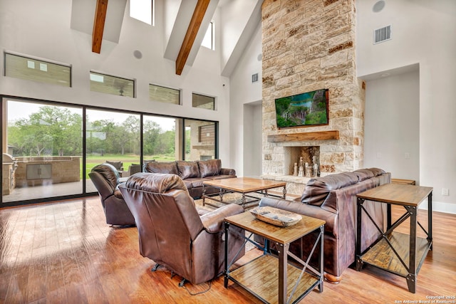 living room featuring beamed ceiling, high vaulted ceiling, a fireplace, and light hardwood / wood-style floors