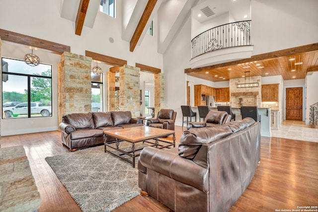 living room featuring decorative columns, a towering ceiling, beam ceiling, and light hardwood / wood-style flooring