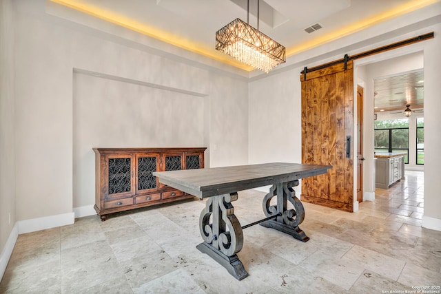 dining space with a barn door, a notable chandelier, and a tray ceiling