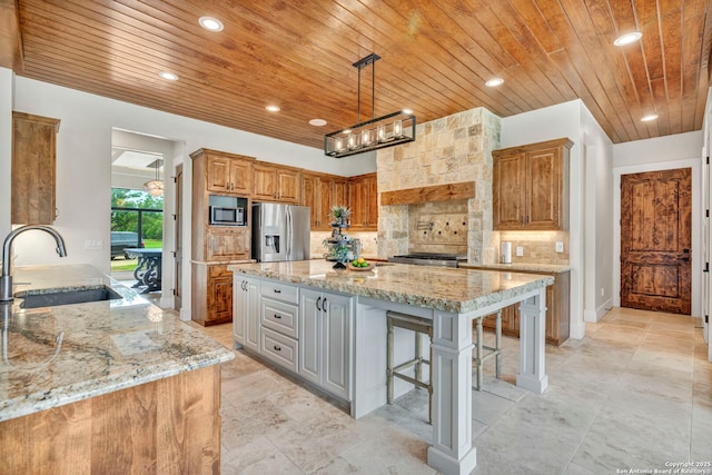 kitchen with sink, a kitchen bar, light stone counters, stainless steel appliances, and a spacious island