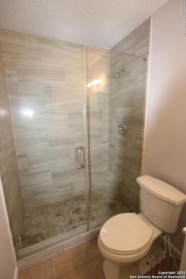 bathroom with tile patterned floors, toilet, a shower with door, and a textured ceiling