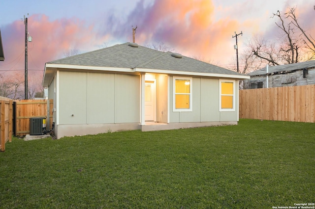 back house at dusk with a yard and central AC