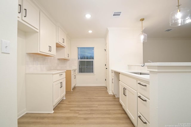 kitchen featuring crown molding, sink, hanging light fixtures, and white cabinets