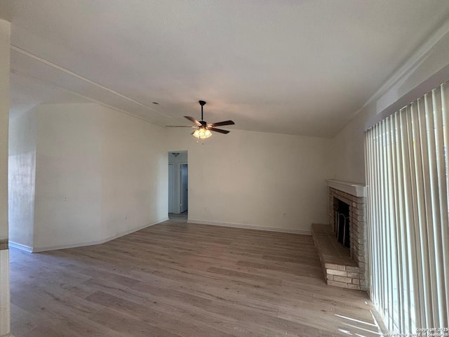 unfurnished living room with ceiling fan, a brick fireplace, lofted ceiling, and light wood-type flooring