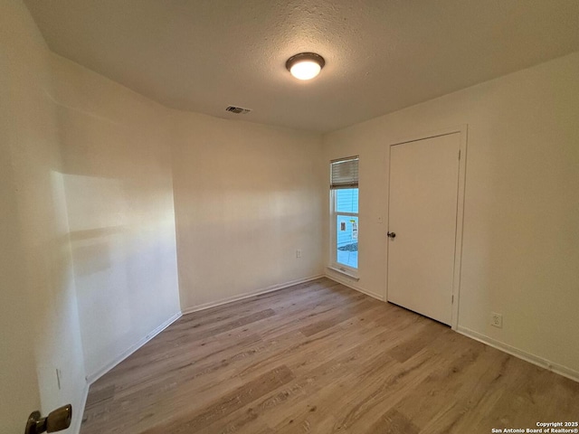 spare room with a textured ceiling and light hardwood / wood-style flooring