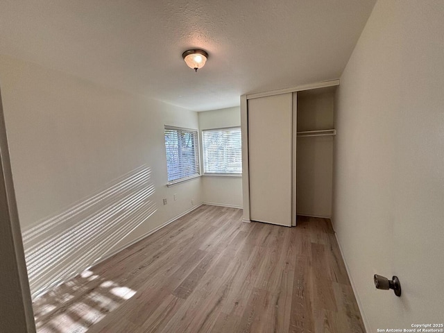 unfurnished bedroom featuring a closet, a textured ceiling, and light hardwood / wood-style flooring