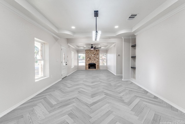 unfurnished living room featuring a fireplace, ceiling fan, a raised ceiling, crown molding, and light parquet floors