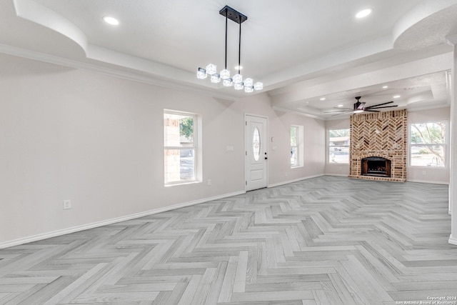 unfurnished living room featuring a brick fireplace, a tray ceiling, and ceiling fan with notable chandelier