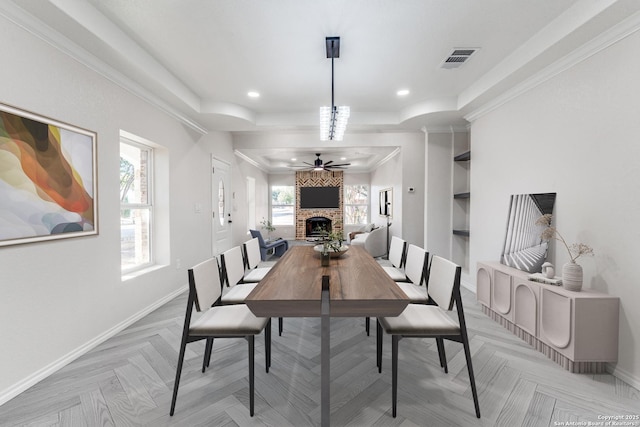 dining area featuring a large fireplace, a raised ceiling, light parquet flooring, and a healthy amount of sunlight