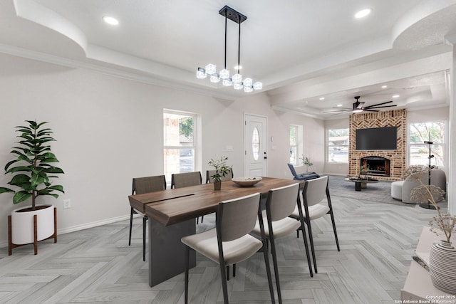 dining room featuring a brick fireplace, light parquet flooring, ceiling fan, a raised ceiling, and ornamental molding