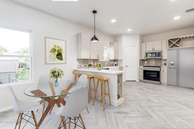 kitchen featuring a kitchen breakfast bar, stainless steel appliances, pendant lighting, white cabinetry, and kitchen peninsula