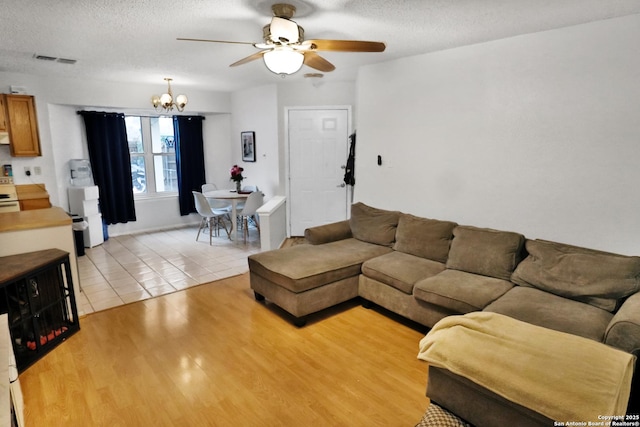 living room featuring ceiling fan with notable chandelier, light hardwood / wood-style floors, and a textured ceiling