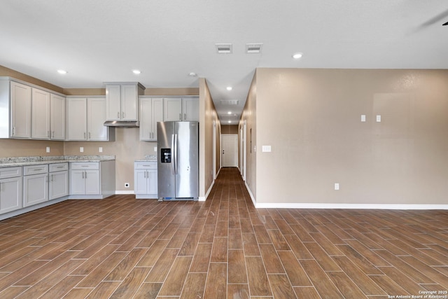 kitchen with light stone counters, stainless steel fridge, and white cabinets