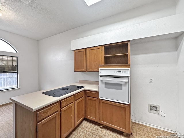 kitchen with black electric cooktop, kitchen peninsula, white oven, and a textured ceiling