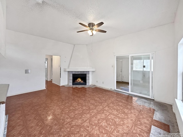 unfurnished living room featuring ceiling fan, a tile fireplace, and a textured ceiling