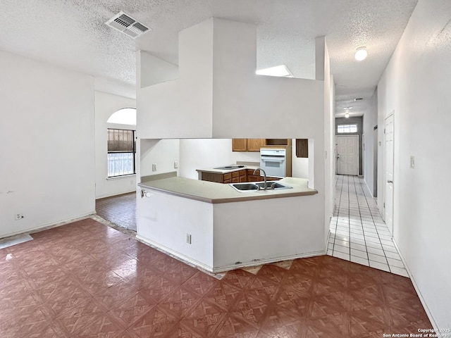 kitchen with sink, kitchen peninsula, a textured ceiling, and white oven