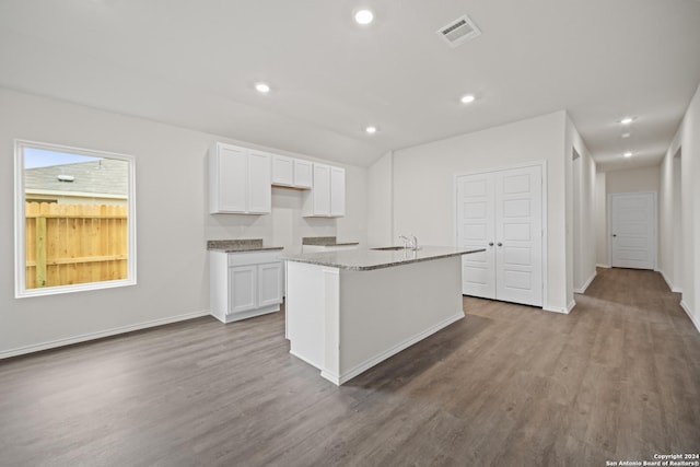 kitchen featuring light hardwood / wood-style flooring, sink, white cabinets, light stone countertops, and a kitchen island with sink