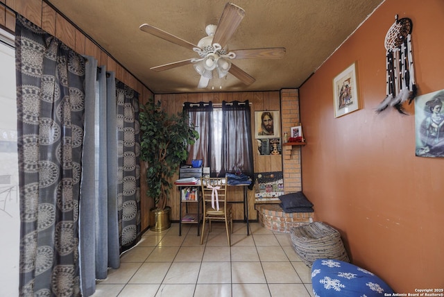 home office featuring ceiling fan, light tile patterned flooring, a textured ceiling, and wooden walls