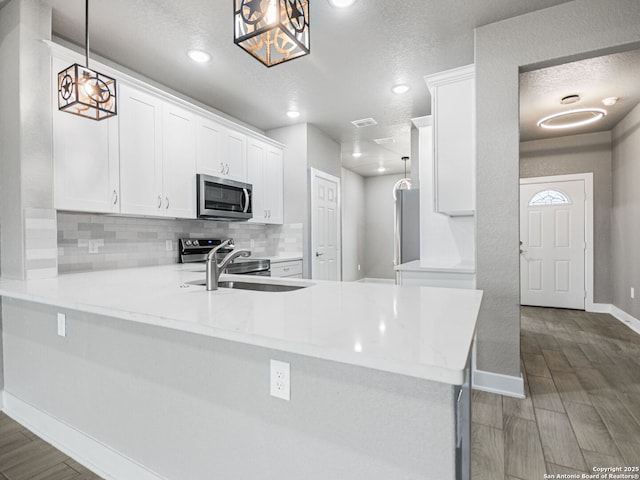 kitchen with sink, pendant lighting, stainless steel appliances, kitchen peninsula, and white cabinets