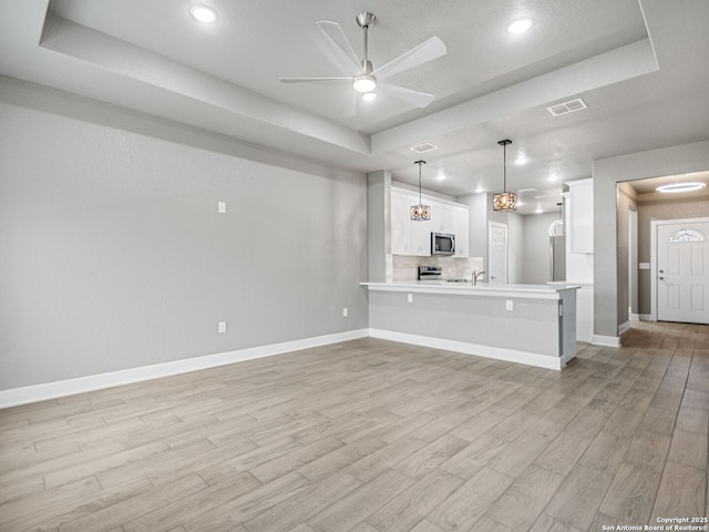 kitchen with appliances with stainless steel finishes, decorative light fixtures, a tray ceiling, white cabinetry, and kitchen peninsula