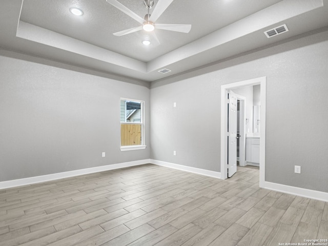 unfurnished room featuring a raised ceiling, light hardwood / wood-style flooring, and ceiling fan