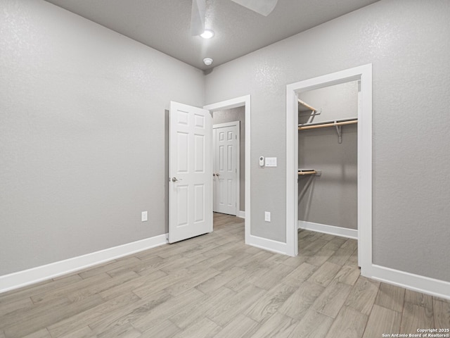 unfurnished bedroom featuring light wood-type flooring, a closet, a walk in closet, and ceiling fan