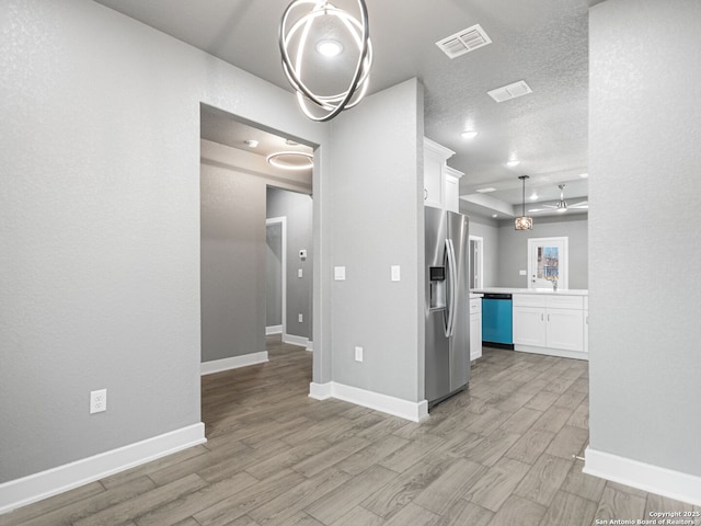 kitchen with light hardwood / wood-style flooring, stainless steel appliances, a textured ceiling, white cabinets, and decorative light fixtures