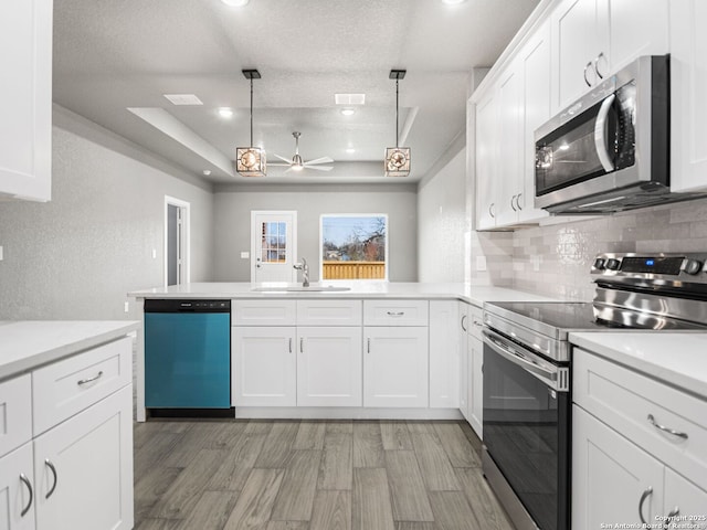 kitchen with white cabinetry, stainless steel appliances, decorative light fixtures, sink, and a raised ceiling