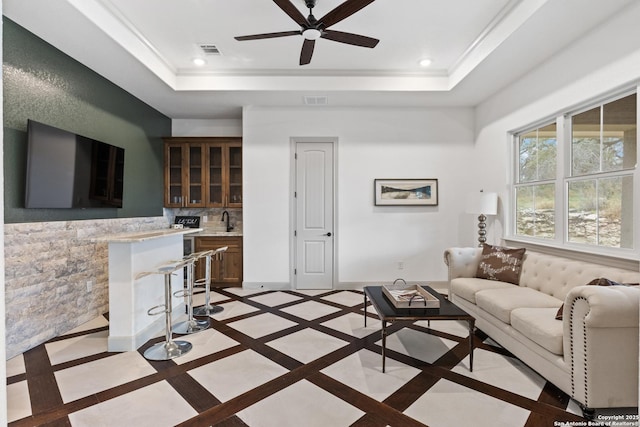 living room with ceiling fan, ornamental molding, sink, and a raised ceiling