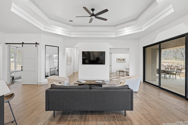 living room with a tray ceiling, a barn door, ceiling fan, and light hardwood / wood-style flooring