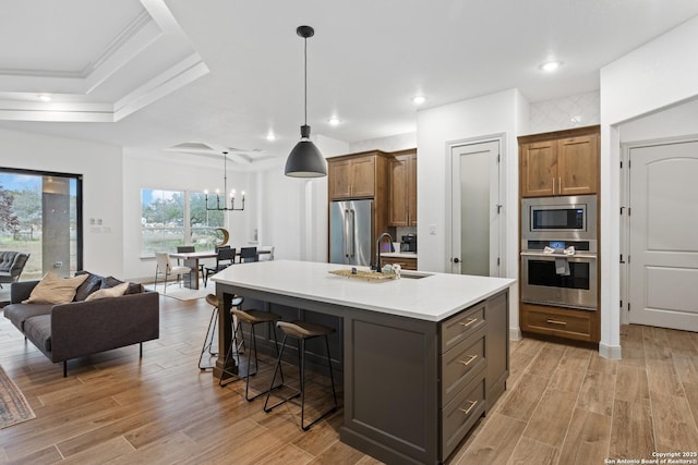 kitchen with appliances with stainless steel finishes, a breakfast bar area, light wood-type flooring, an island with sink, and sink