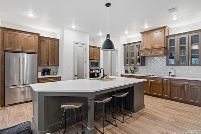 kitchen with a center island with sink, a kitchen bar, sink, stainless steel appliances, and hanging light fixtures