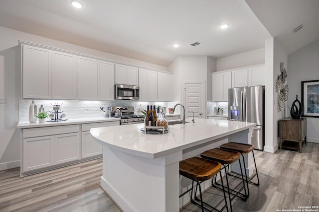 kitchen featuring appliances with stainless steel finishes, a kitchen island with sink, white cabinets, and backsplash