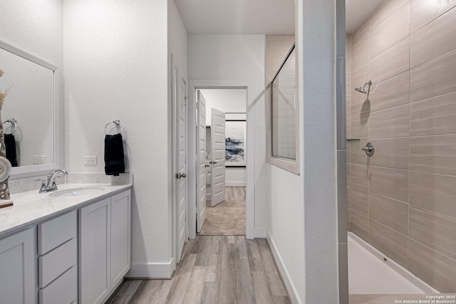 bathroom with hardwood / wood-style flooring, a tile shower, and vanity