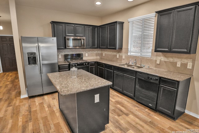 kitchen with light wood-type flooring, a kitchen island, black appliances, light stone countertops, and sink