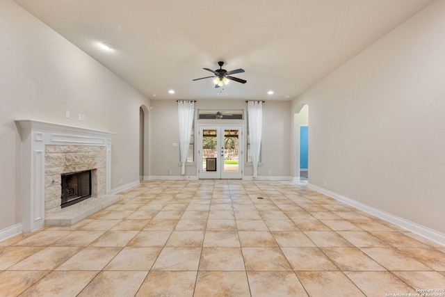 unfurnished living room with light tile patterned floors, arched walkways, a ceiling fan, and baseboards