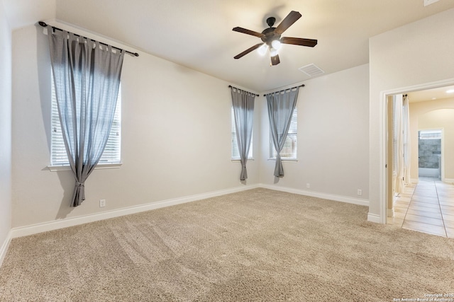 carpeted spare room featuring visible vents, arched walkways, baseboards, ceiling fan, and tile patterned floors