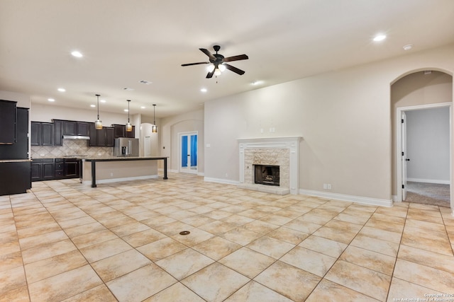 living room featuring a ceiling fan, recessed lighting, arched walkways, and a stone fireplace