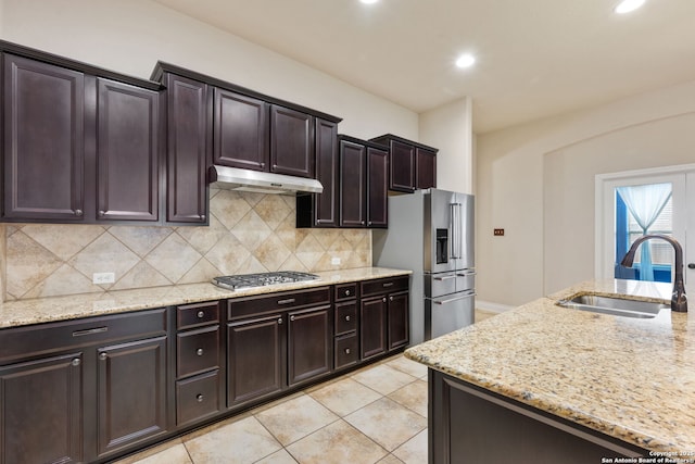 kitchen featuring a sink, light stone countertops, stainless steel appliances, under cabinet range hood, and backsplash