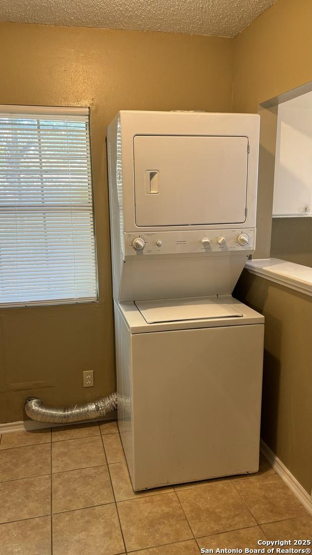 clothes washing area with light tile patterned flooring, a textured ceiling, and stacked washing maching and dryer