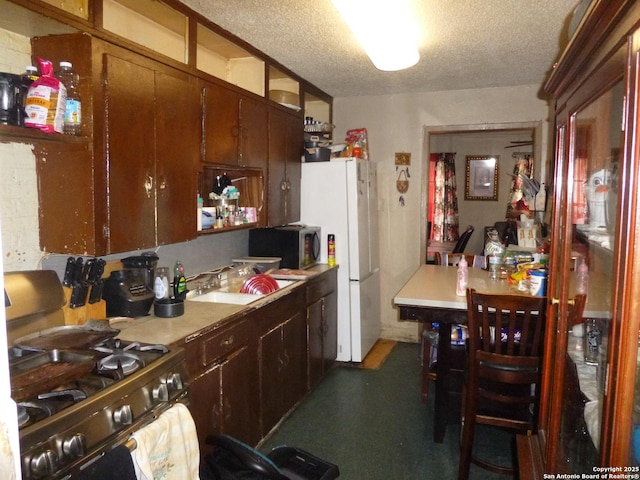 kitchen with a textured ceiling, white refrigerator, sink, and gas range