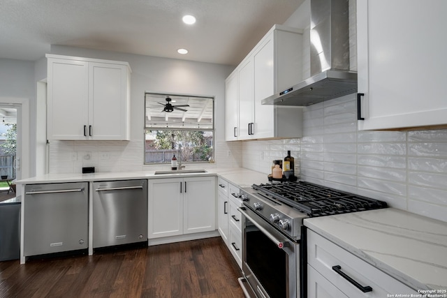 kitchen with appliances with stainless steel finishes, sink, wall chimney exhaust hood, and white cabinetry