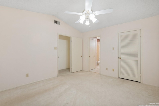 unfurnished bedroom featuring light carpet, visible vents, a ceiling fan, ensuite bath, and vaulted ceiling