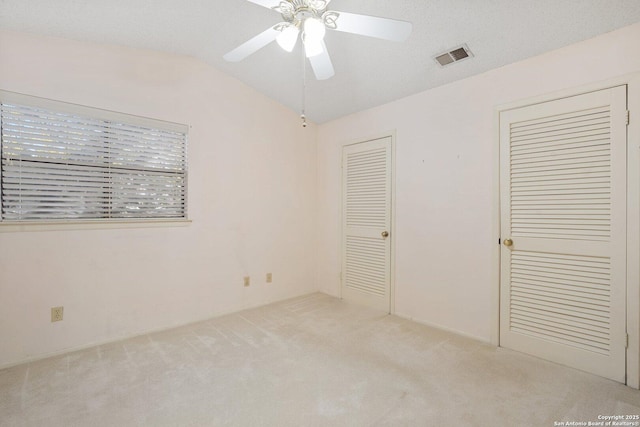 unfurnished bedroom with lofted ceiling, ceiling fan, light carpet, and visible vents