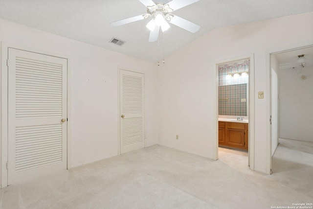 unfurnished bedroom with lofted ceiling, light colored carpet, visible vents, ensuite bathroom, and a sink